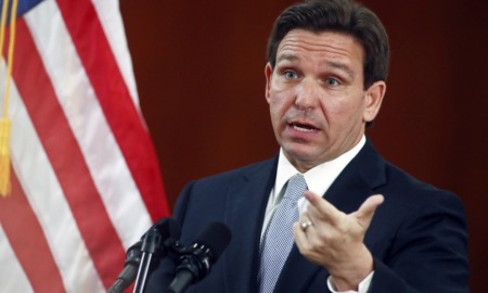 DeSantis to expand 'Don't Say Gay' law to all grades: white man with brown hair talking at podium while gesturing with hand