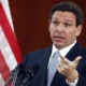 DeSantis to expand 'Don't Say Gay' law to all grades: white man with brown hair talking at podium while gesturing with hand