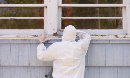 EPA proposes lower lead exposure limit in daycares, homes: person in hazmat suit painting the exterior window sill of older home