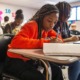 How one district has diversified math classes without the controversy: young black female student in classroom works at desk on paper while another student is on laptop next to her