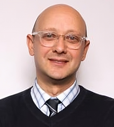 Immigrant student school admissions: Bald white man with wire glasses in dark sweater pullover with light plaid shirt and dark tie